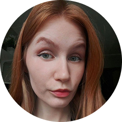 Close-up portrait of a young woman with red hair and green eyes, looking at the camera with a neutral expression.
